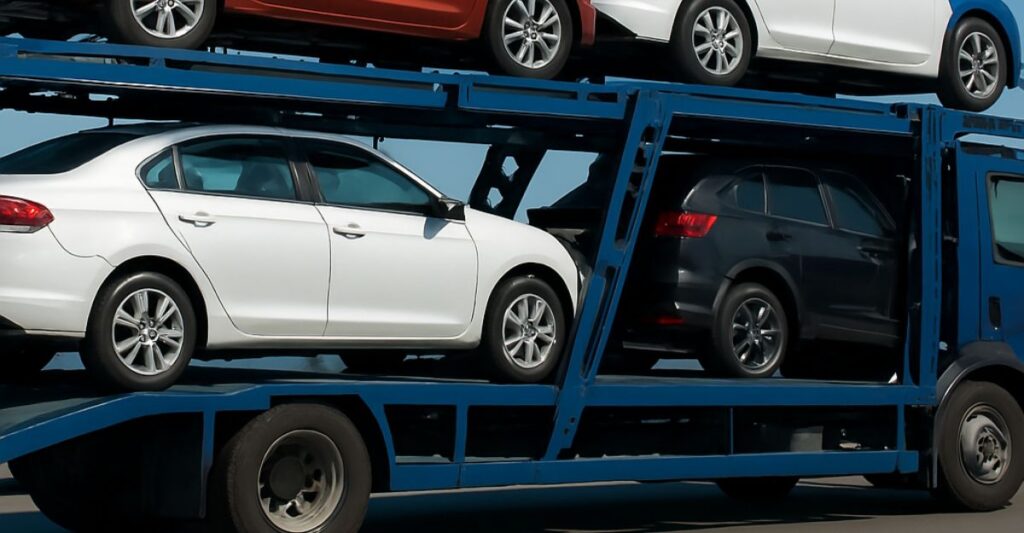 Open car carrier transporting multiple vehicles on a highway under clear blue sky.